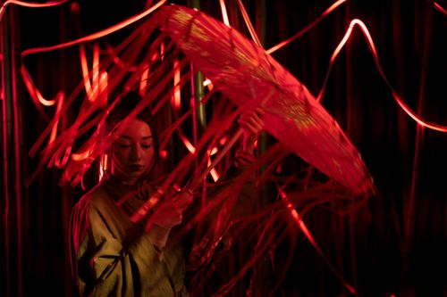 Free A woman in traditional attire poses with a paper umbrella amid vibrant red lights. Stock Photo