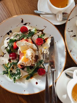 A delicious breakfast of poached eggs, cherry tomatoes, and arugula on a plate with cutlery, shot from above.