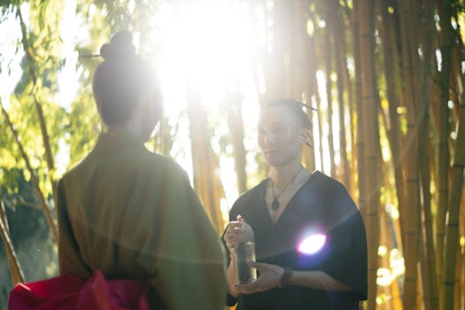 Two people in traditional attire engage in a serene moment within a bamboo forest.