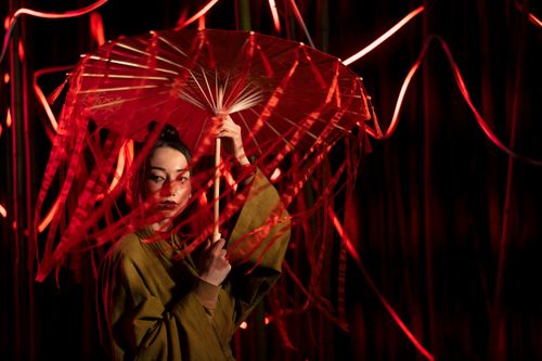 Free Artistic portrait of a Japanese woman in a kimono holding a parasol amidst vibrant red lights. Stock Photo