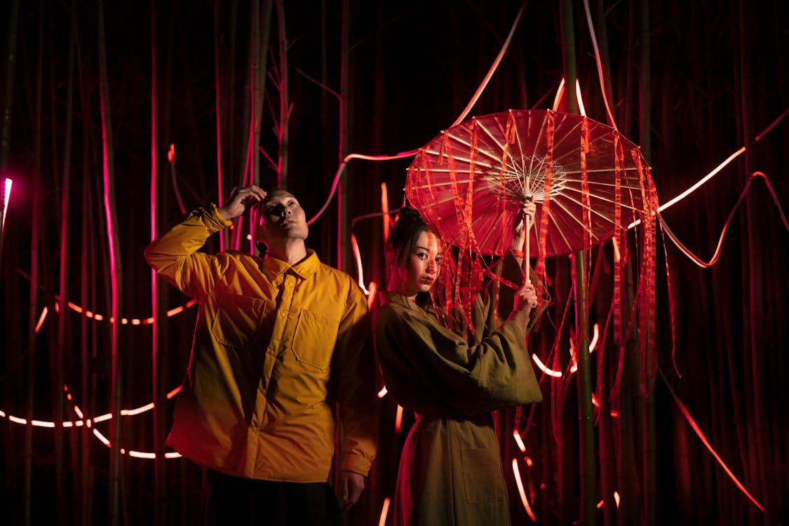 Two people standing and posing on stage with red curtains.