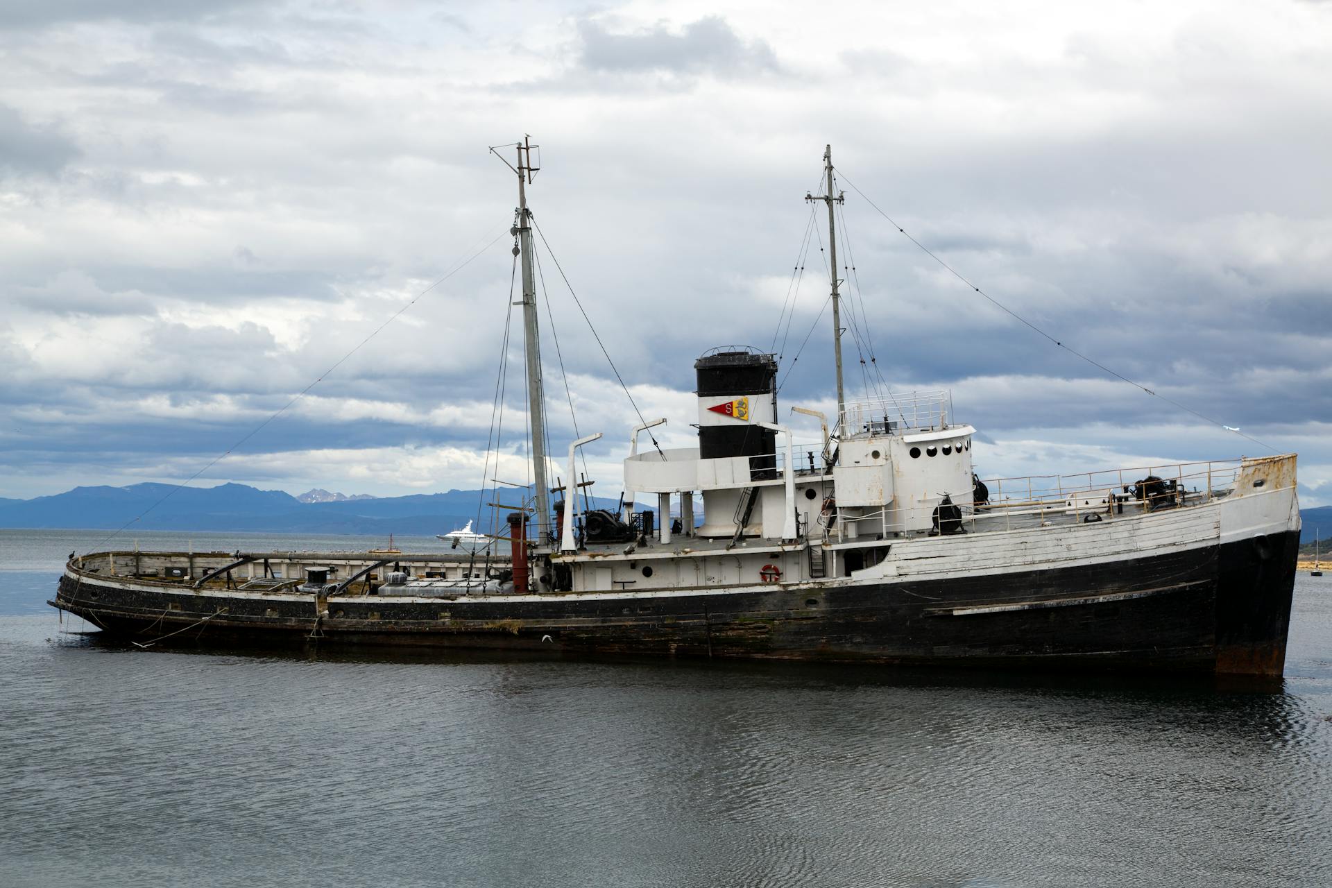A vintage ship anchored in a peaceful harbor under a cloudy sky.