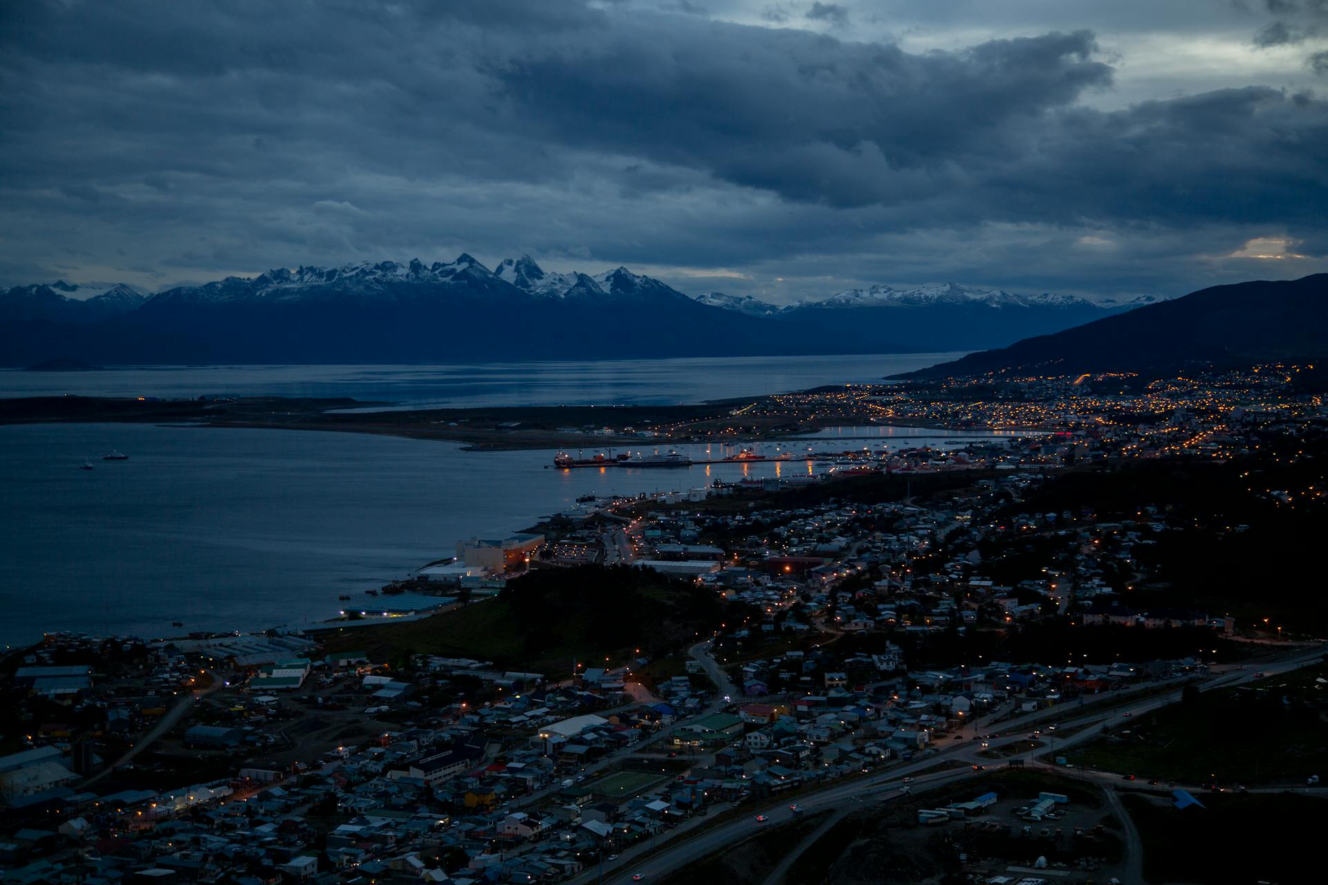 Aerial view of Ushuaia city at night with twinkling lights and picturesque mountains in the background.