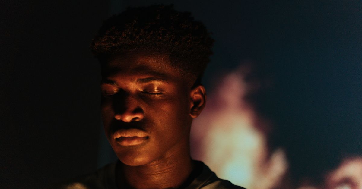 Close-up portrait of an African American man with eyes closed against a blurred warm background.