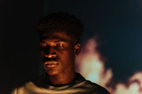 Free Close-up portrait of an African American man with eyes closed against a blurred warm background. Stock Photo