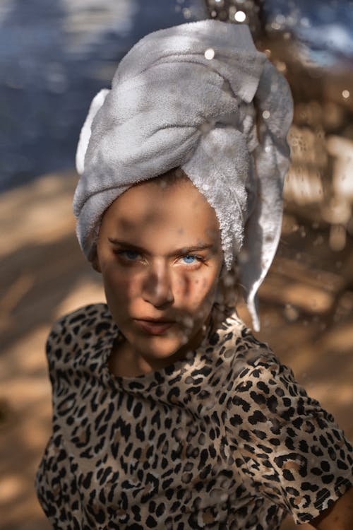 Young woman with terry towel on head and shades on face looking at camera in sun rays on blurred background