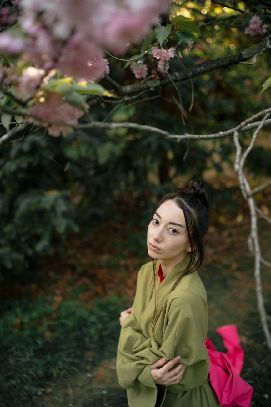 A woman in a green kimono gazes thoughtfully under blooming cherry blossoms, embodying traditional Japanese aesthetics.
