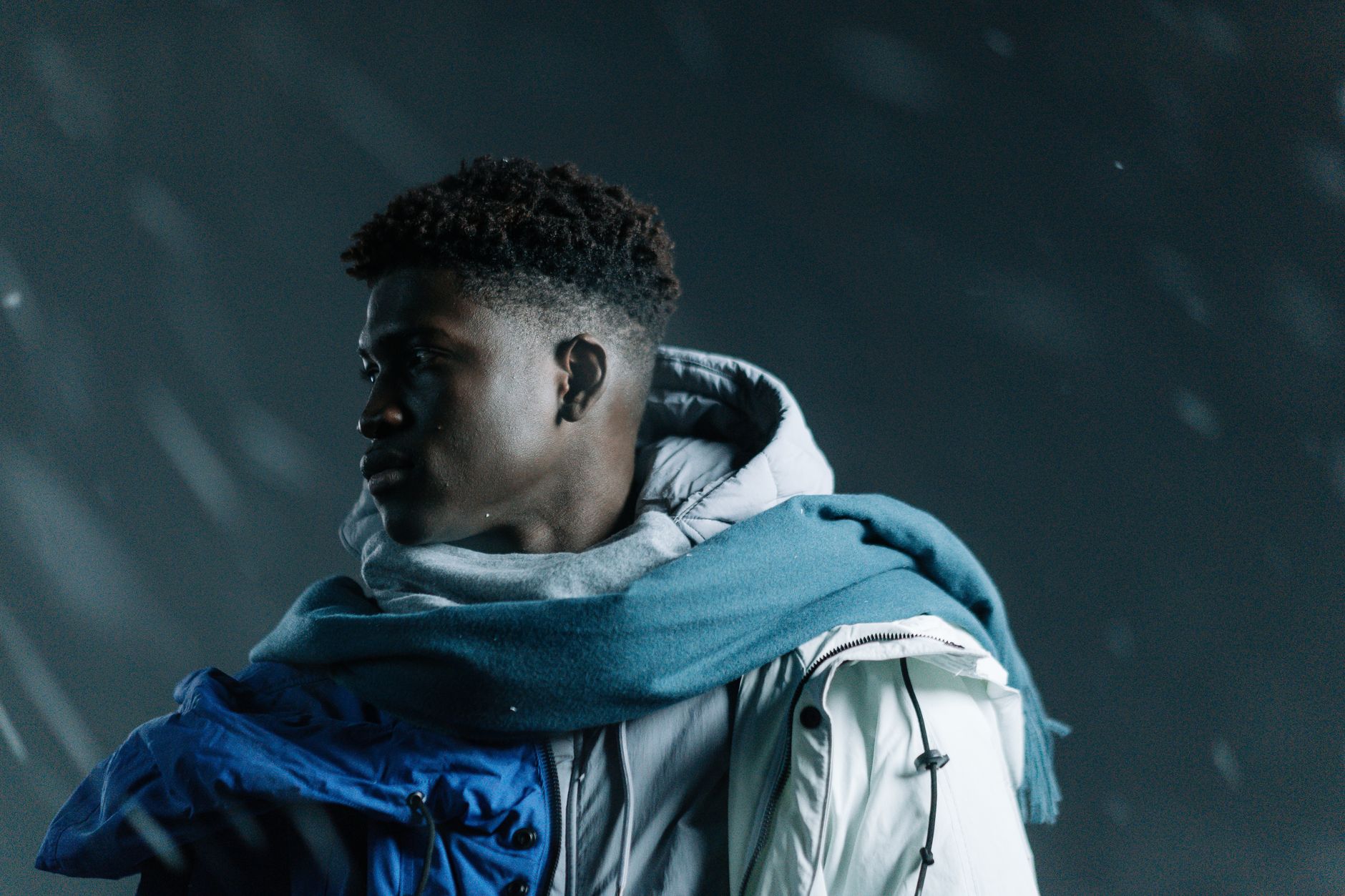 A young man in winter clothing looks away while standing in a snowstorm.