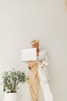 Confident woman in a stylish blazer holding a laptop indoors, exemplifying modern business leadership.