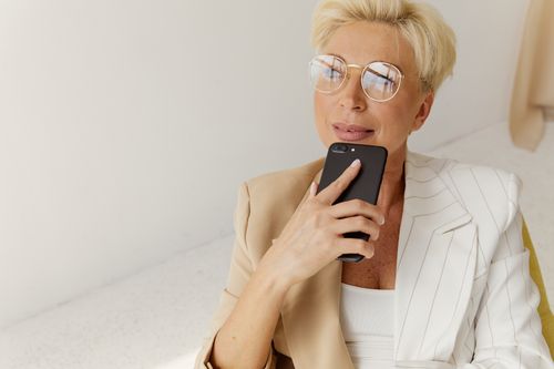 Free Confident businesswoman in glasses holding smartphone, relaxing indoors. Stock Photo