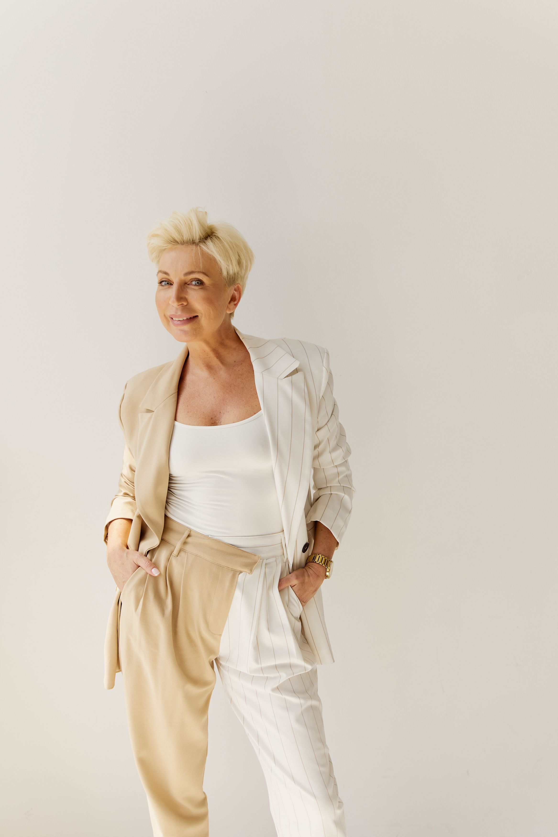 Smiling businesswoman in a stylish two-tone beige and white suit poses confidently indoors.