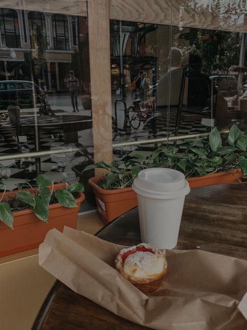 Free Warm cafe setting with takeaway cup, dessert, and view of the street through large windows. Stock Photo