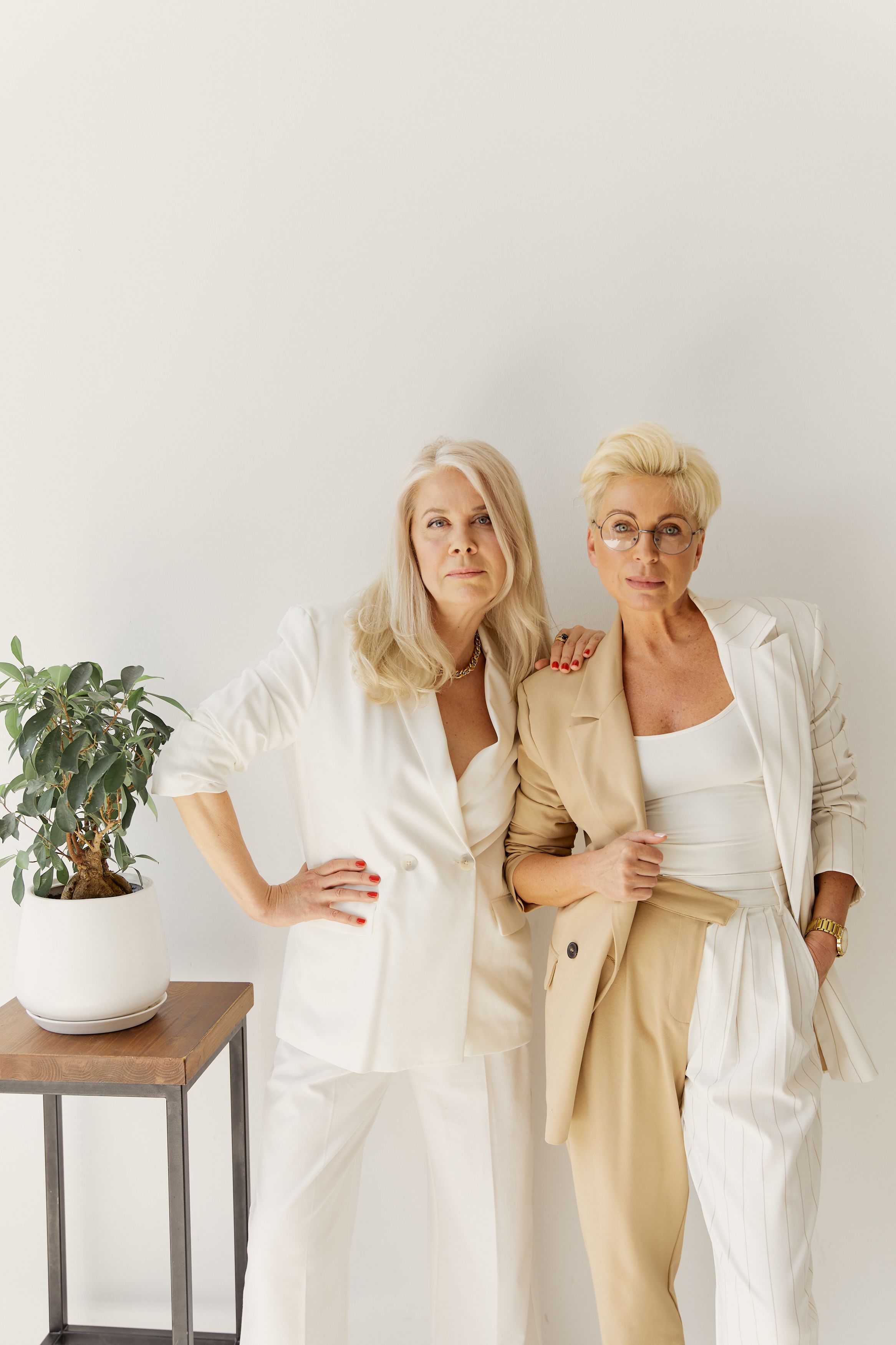 Two stylish middle-aged women posing confidently in chic business attire, embodying modern professionalism.