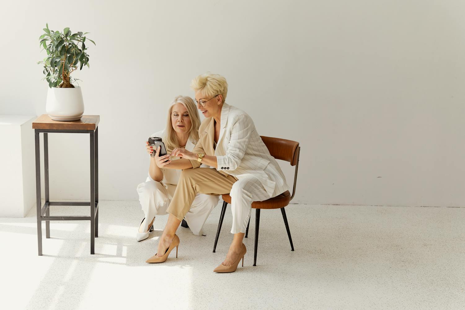 Two stylish women discussing business strategy in a modern, minimalist office setting.