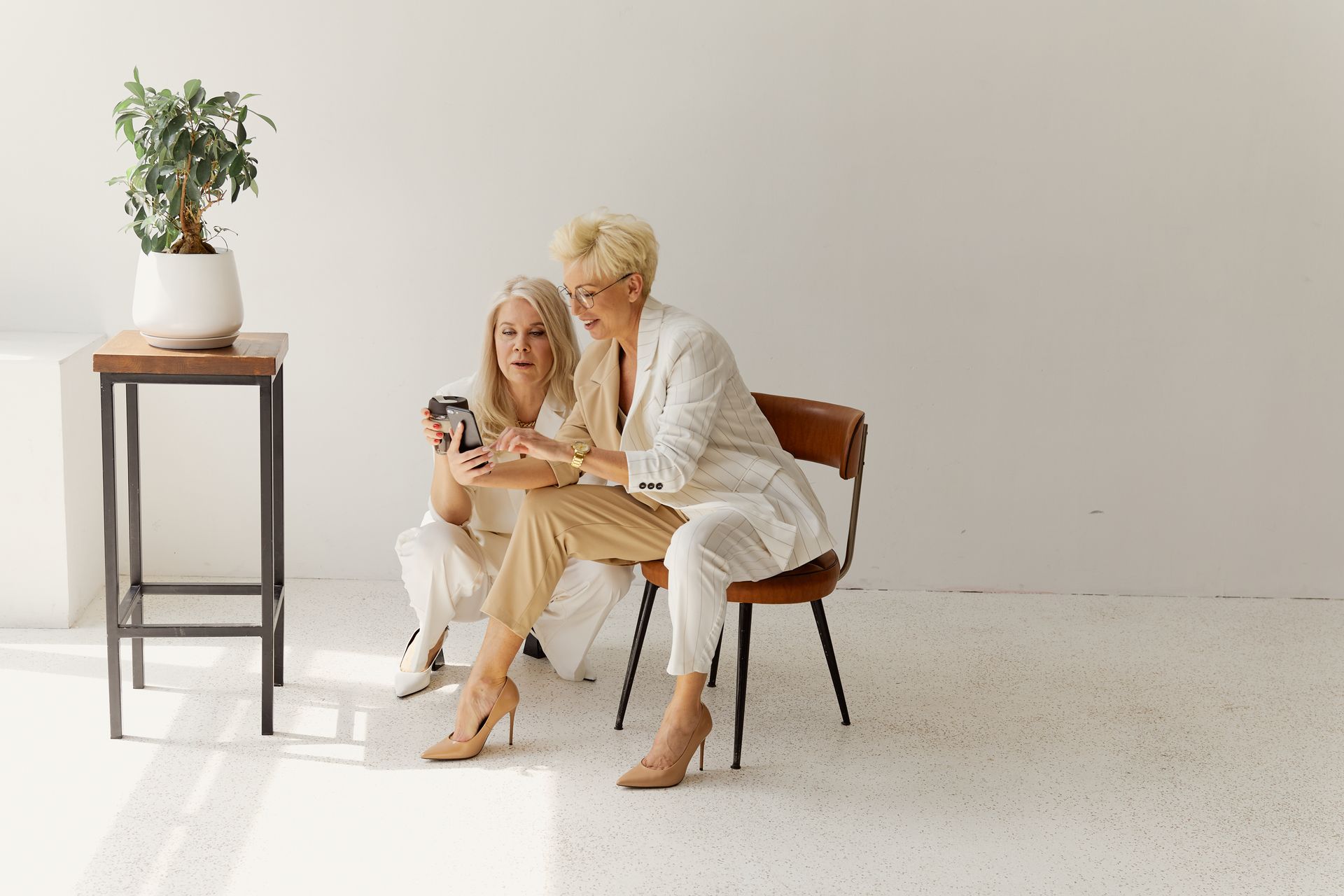 Two stylish women discussing business strategy in a modern, minimalist office setting.