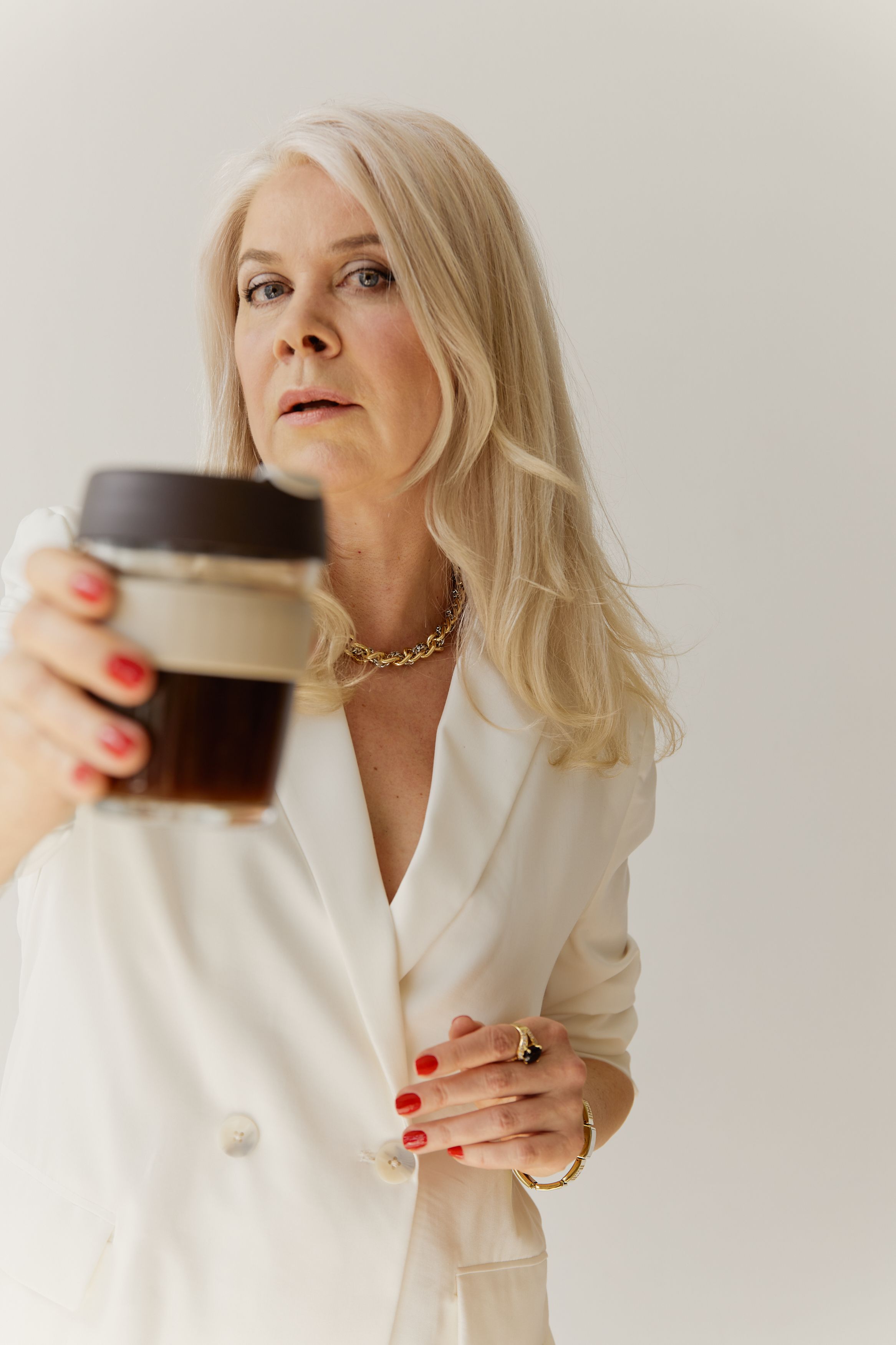 Elegant woman in white, holding a cup of coffee indoors. Stylish and poised.