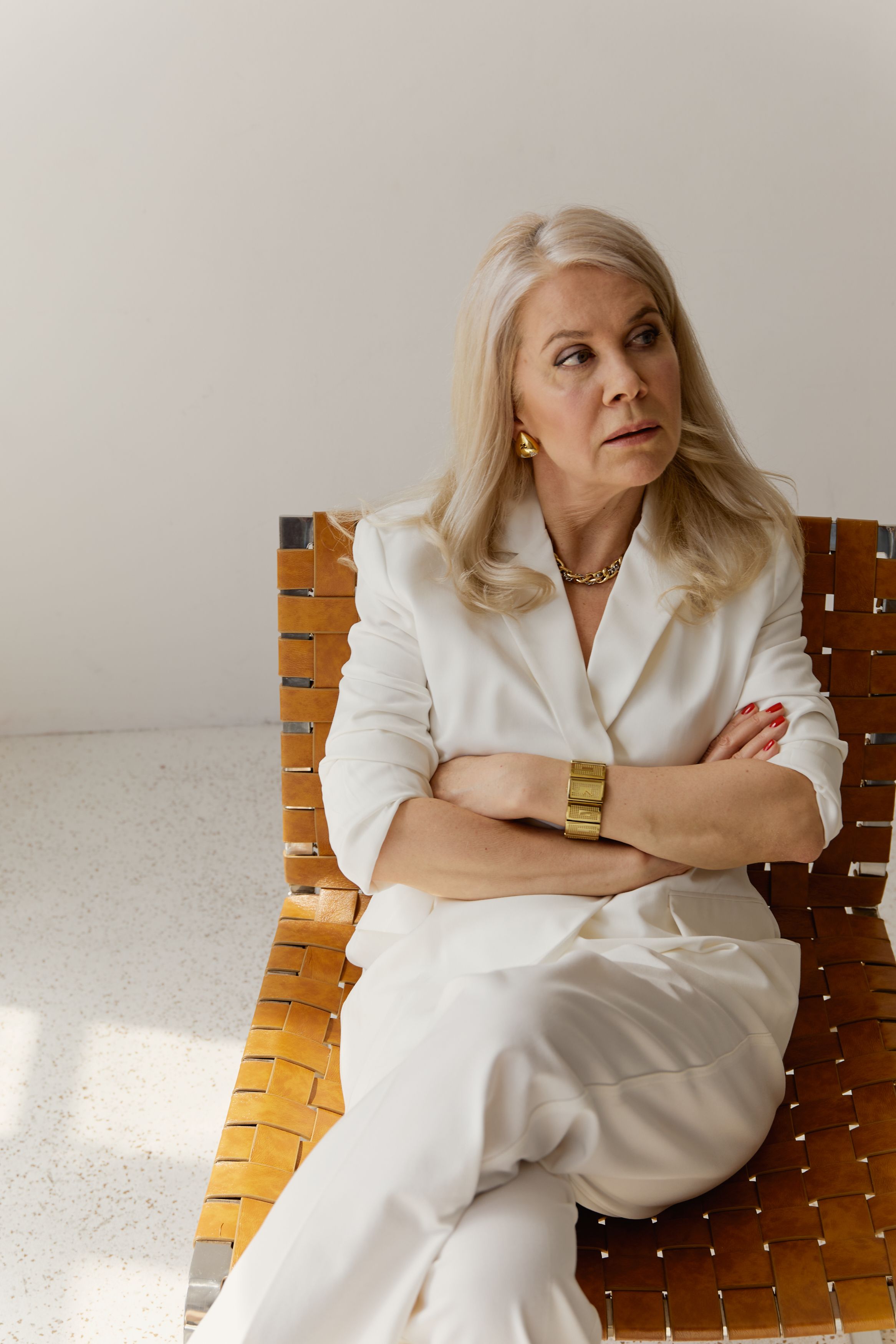 Senior woman in elegant white business suit sitting on a modern chair indoors. Professional and thoughtful.