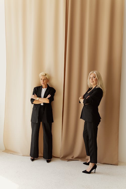 Two Women Wearing Black Long Sleeve Shirt Standing Beside Brown Curtain