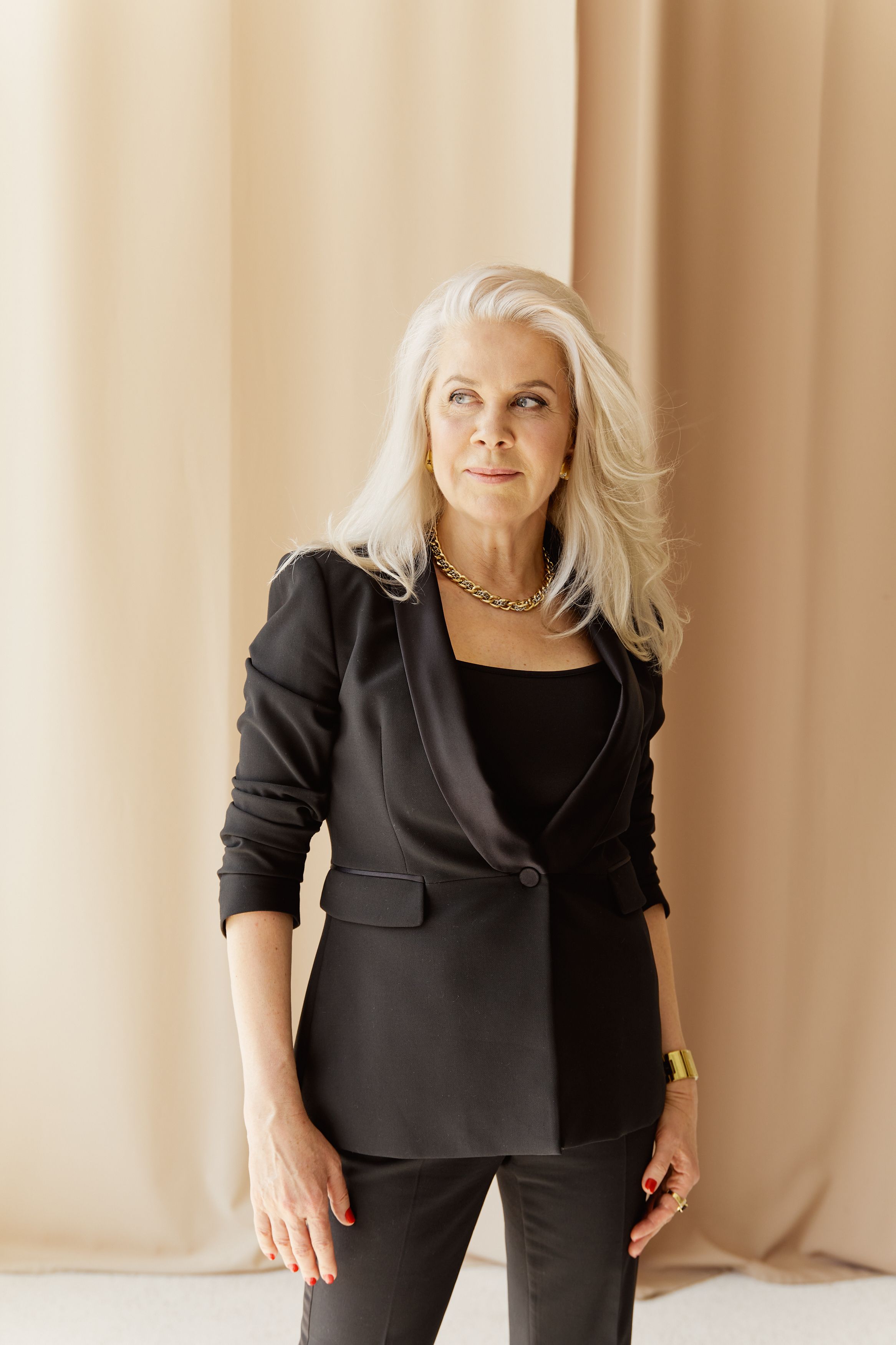 Sophisticated portrait of a stylish senior woman in a black suit with blonde hair and chain necklace.