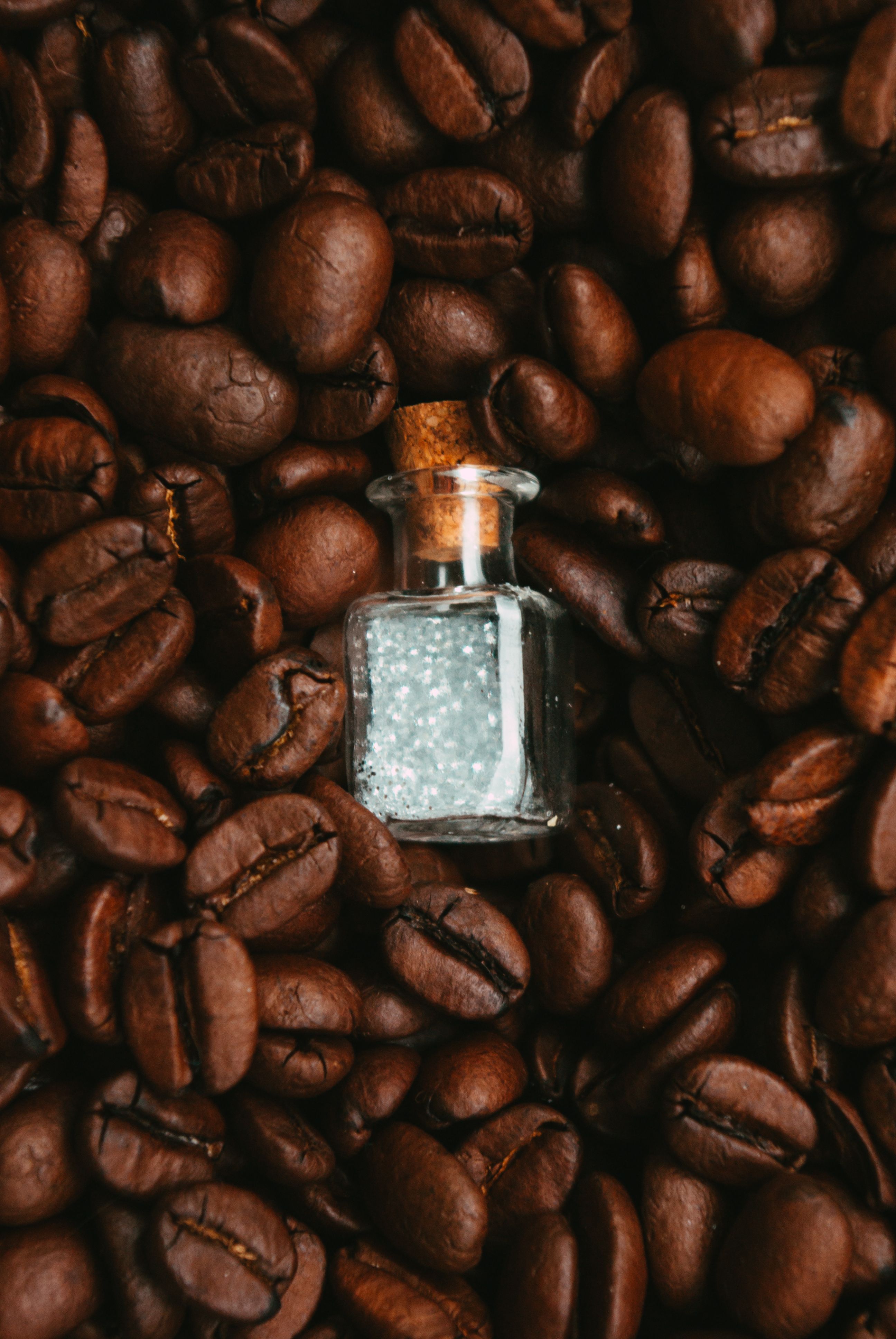 A clear bottle of sambuca next to a small glass with three coffee beans floating on top, the traditional way it's served.