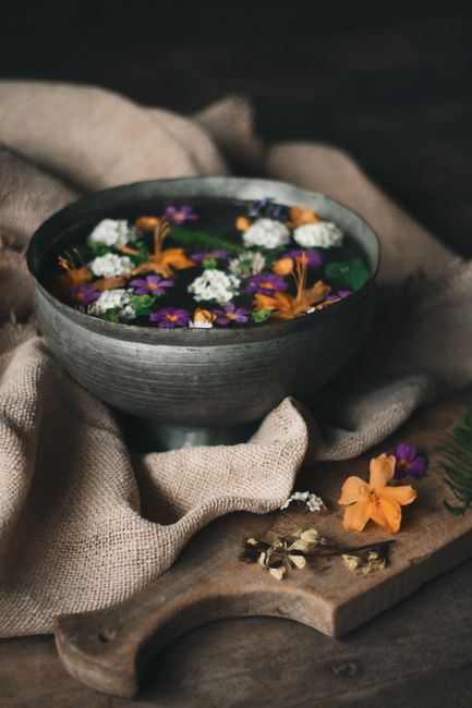 High angle of bowl with flower blossoms and water placed on blanket near cutting board with dried buds and leaves
