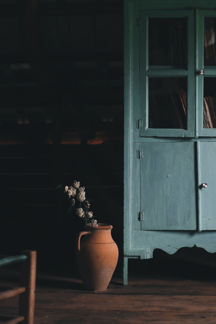 Vintage Cupboard And Clay Vase With Flowers In Semidarkness