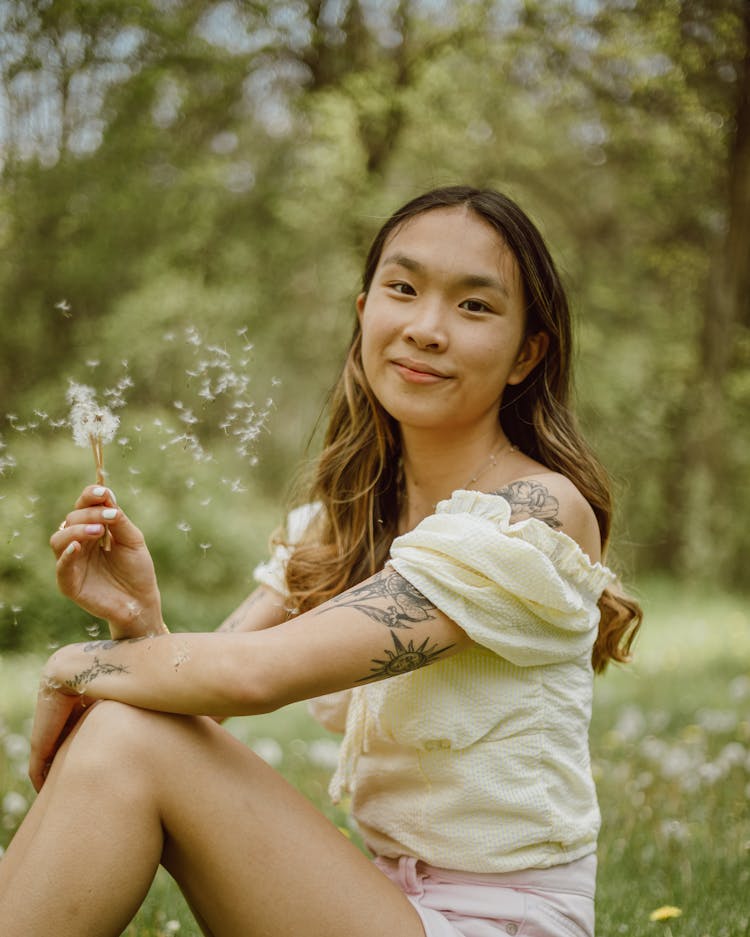 Smiling Asian Woman Blowing Dandelion In Nature