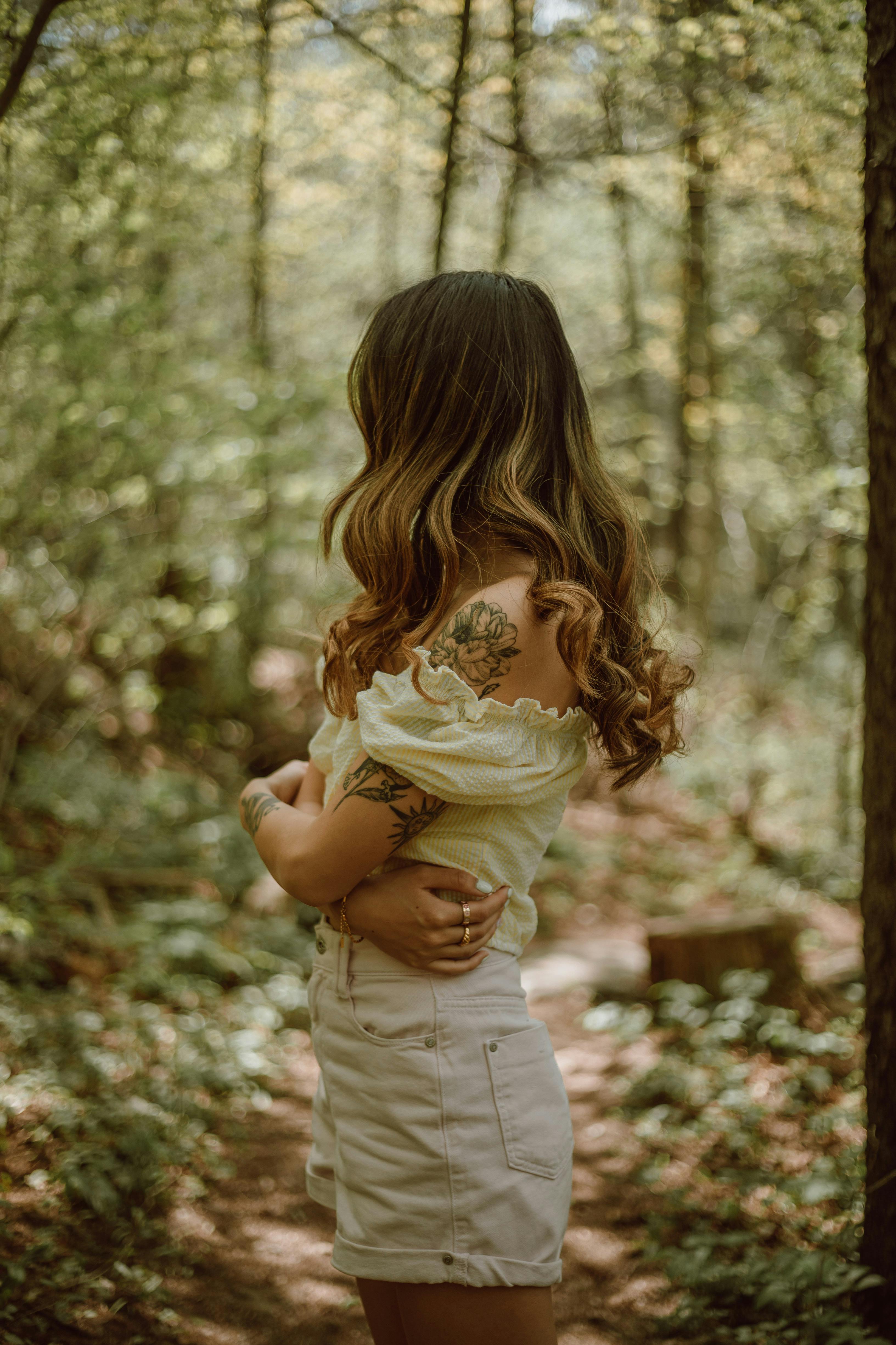 Side view of faceless female hugging herself standing on footpath in woods in sunny day