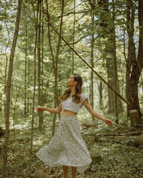 Free Relaxed ethnic female with outstretched arms spinning around among plants growing in dense woodland Stock Photo
