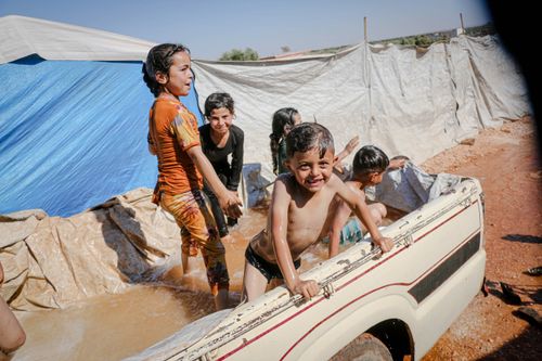 Free Joyful Syrian children beat the heat by playing in a makeshift pool in Idlib camp. Stock Photo