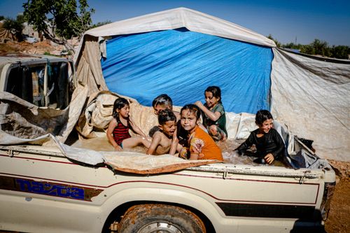 Free A group of happy children plays in a makeshift pool in a pickup truck under a tarp outdoors. Stock Photo