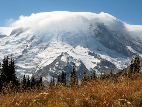 Stunning view of Mount Rainier with snow cap and clouds under a clear blue sky.