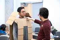 Man measuring his Colleague while wearing Cut-out Carton Boxes