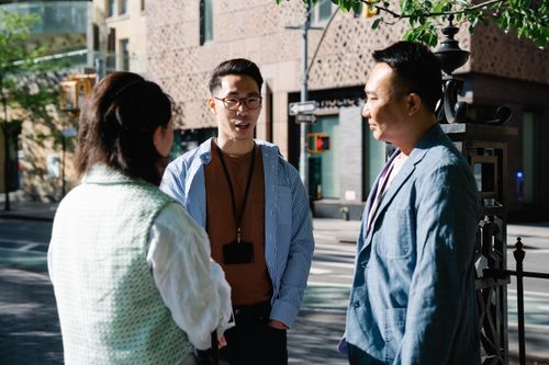Free Three professionals engaged in conversation outdoors in a city backdrop. Stock Photo