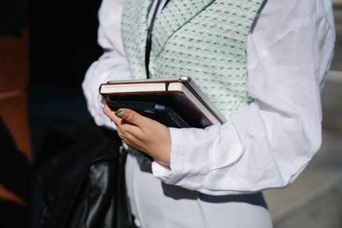 Free A stylish individual in a white shirt holding a notebook and tablet outdoors. Stock Photo