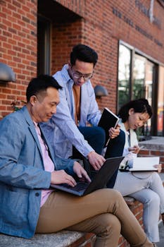 Group of professionals collaborating with laptops and notebooks outside a brick building.