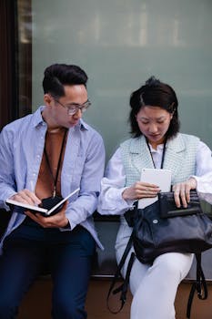 Two young adults collaborating with digital devices outdoors, focused and engaged.
