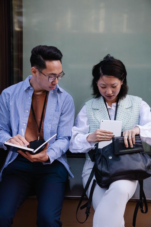 Free Two young adults collaborating with digital devices outdoors, focused and engaged. Stock Photo