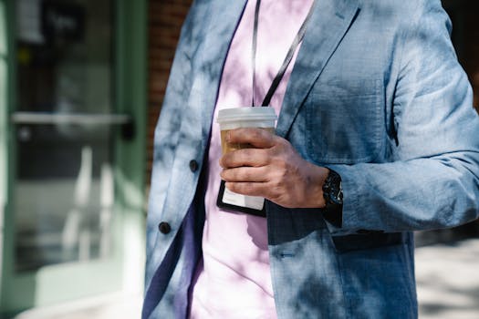 A professional man in a blue blazer holds a coffee cup outside a building.
