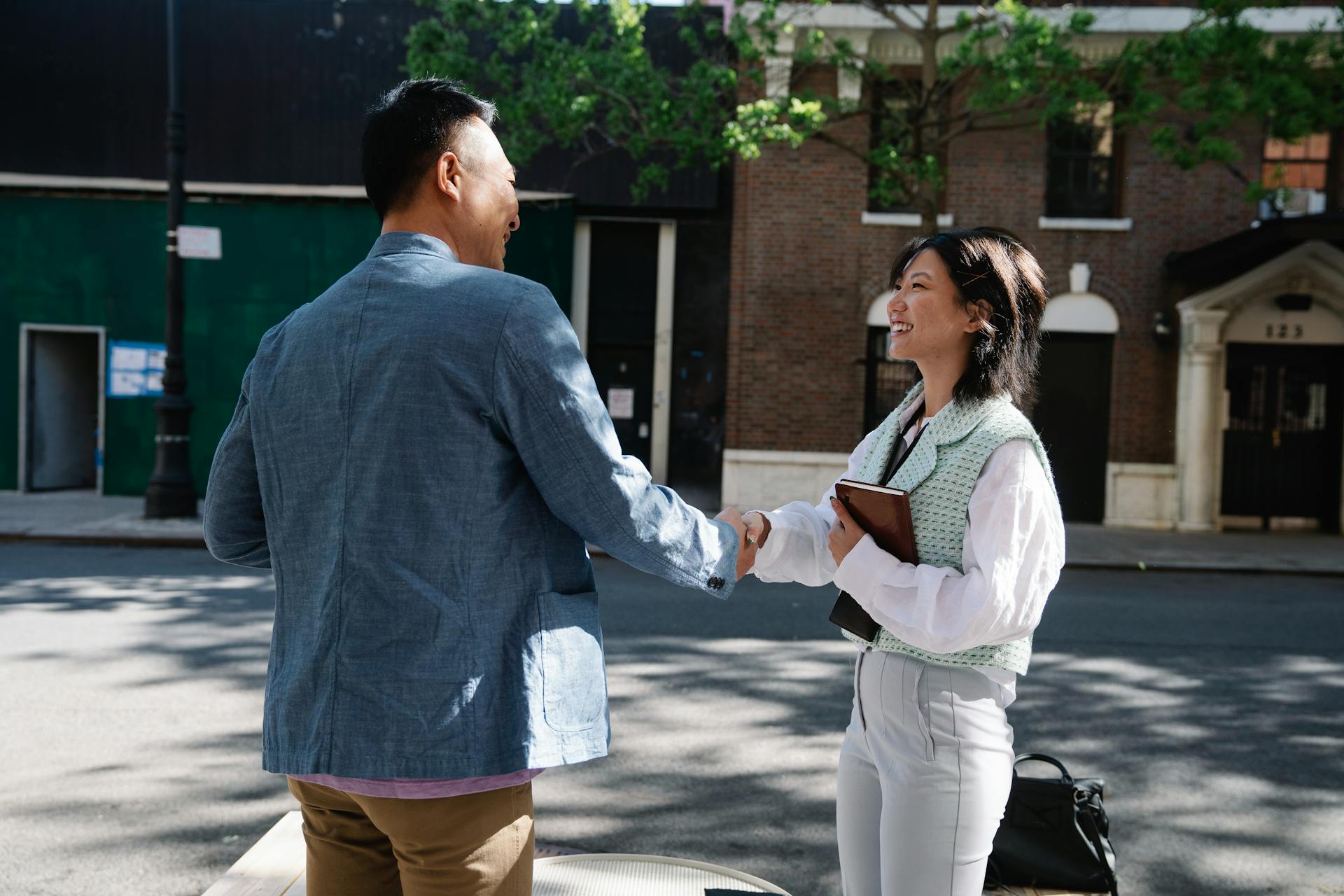 Two adults having a friendly business handshake outdoors in a city setting.