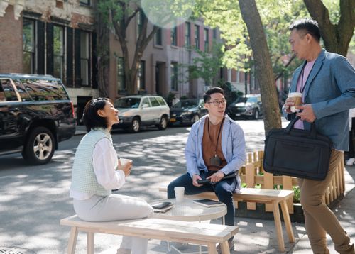 Free Three colleagues enjoying a coffee break on a shaded city street, engaging in conversation. Stock Photo