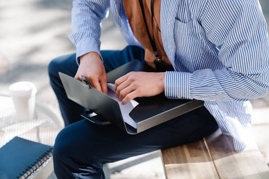 Professional reviewing documents in a folder while sitting outside, dressed in business attire.