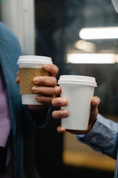 Two people holding takeaway coffee cups on a train, showcasing a daily commute.