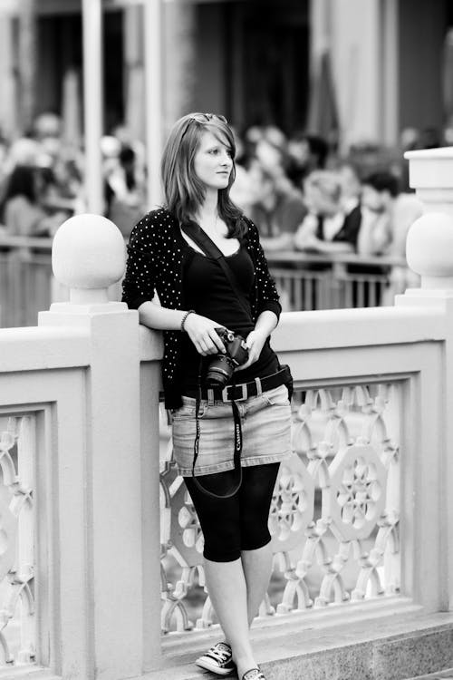 Woman Holding a Camera Leaning on Concrete Railing