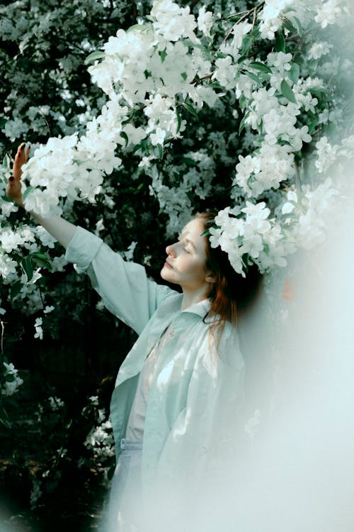 Free High angle of lady standing under blossoming tree in garden and closing eyes Stock Photo