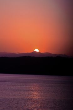 Serene sunset with vibrant colors over water and mountain silhouette.