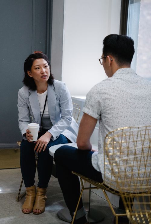 Free Two adults engaged in a casual conversation in a modern café setting, with coffee in hand. Stock Photo