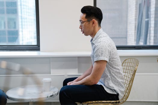 A man in a casual shirt sitting at a marble table with a coffee cup, indoors.