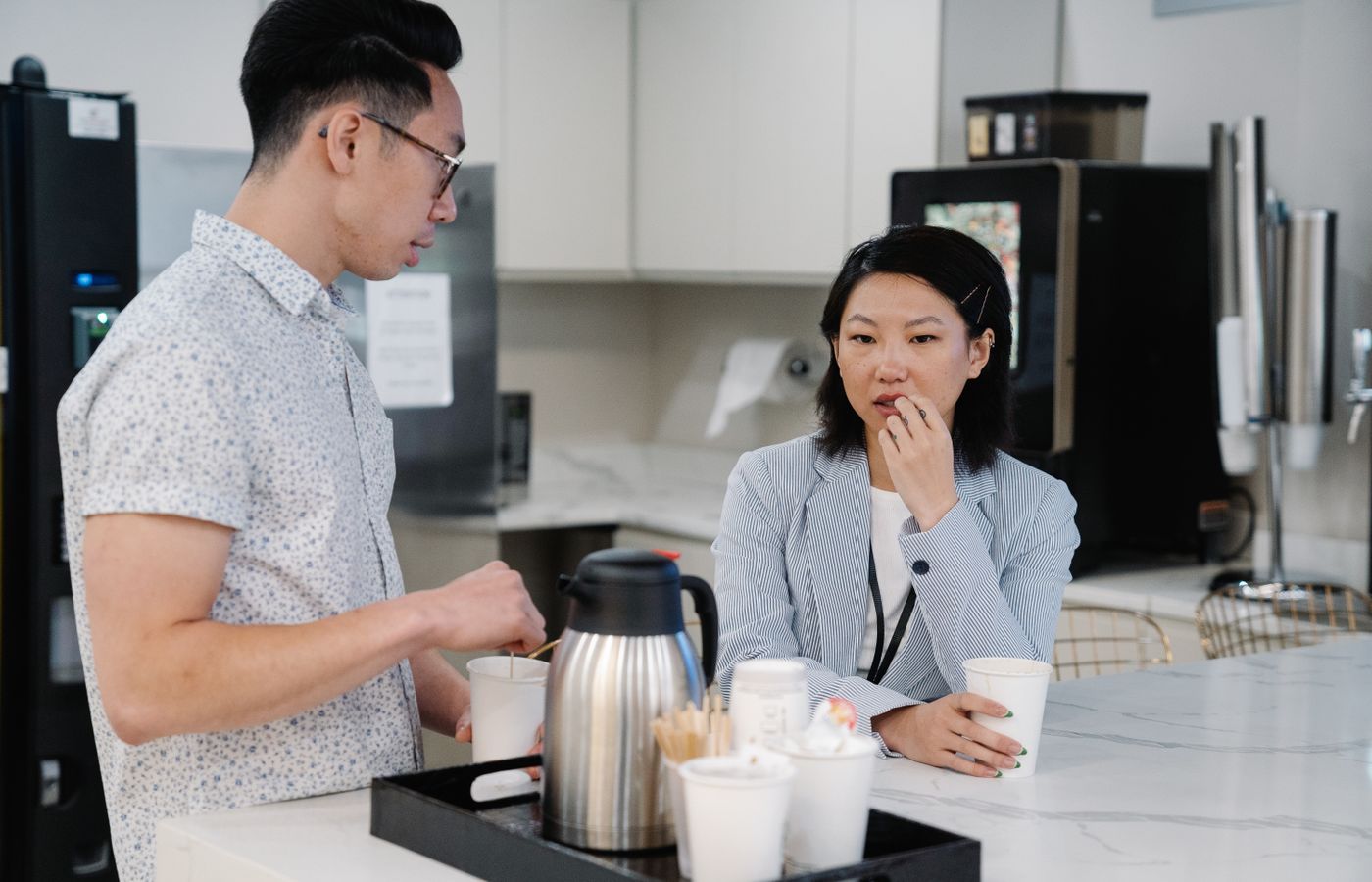 Two colleagues discussing over coffee in a modern office break room setting.