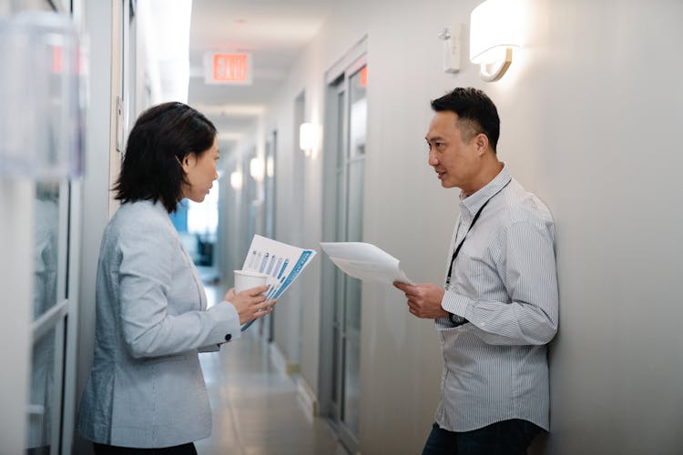 Man And Woman Talking In The Hallway While Holding Papers